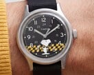 Крупный план чёрного циферблата часов Timex MK1, на котором изображён Снупи на фоне жёлто-чёрной клетчатой графики с арабскими часовыми метками и светящимися стрелками.
