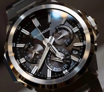Крупный план часов Casio G-Shock GST-W1000D-1A с чёрным циферблатом, на котором видны три дополнительных циферблата, светящиеся часовые метки, граненые стрелки и безель из нержавеющей стали с многослойной отделкой.