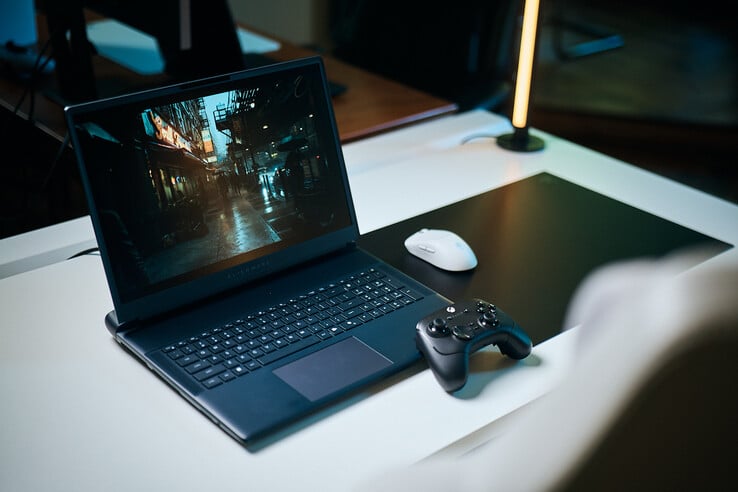 Открытый игровой ноутбук Alienware, установленный на белом студийном столе, на экране которого отображается тёмная, отражающая свет уличная сцена с чёткой детализацией, созданной с помощью трассировки пути, в сочетании с чёрным контроллером и белой беспроводной мышью.