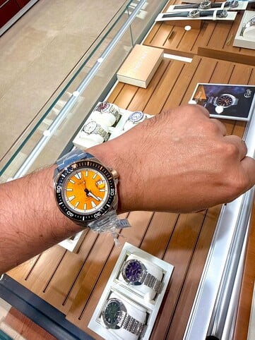 Часы Seiko Prospex HBB005K1 в стиле дайвера, вдохновленные образом тигра, на запястье: на них видны янтарный циферблат с текстурированной поверхностью, чёрный безель с оранжевыми акцентами, а также корпус и браслет из нержавеющей стали.