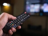 Рука с пультом дистанционного управления на фоне размытого телевизора