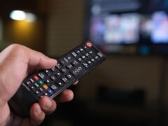Рука с пультом дистанционного управления на фоне размытого телевизора