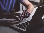 Руки, печатающие на клавиатуре MacBook при слабом освещении; светящийся логотип Apple
