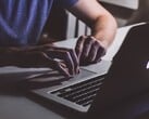 Руки, печатающие на клавиатуре MacBook при слабом освещении; светящийся логотип Apple