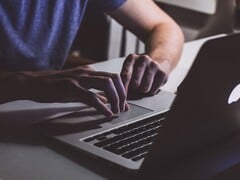 Руки, печатающие на клавиатуре MacBook при слабом освещении; светящийся логотип Apple