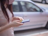 Женщина печатает на смартфоне на фоне серебристого автомобиля