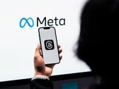 Рука держит смартфон перед большим логотипом Meta