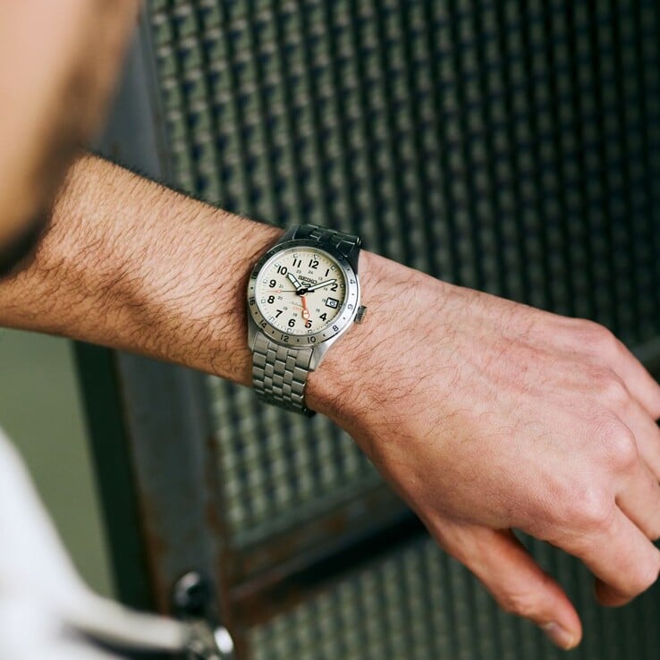 Вид спереди на часы Seiko 5 Sports Field GMT HDB002 с кремовым циферблатом, оранжевой стрелкой GMT, фиксированным 24-часовым безелем и браслетом из нержавеющей стали.
