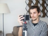 Молодой человек снимает себя дома на смартфон, закреплённый на штативе