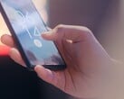 Рука держит смартфон и разблокирует его с помощью датчика отпечатков пальцев на экране блокировки.