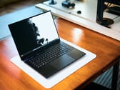 Игровой ноутбук Razer Blade 16 с открытым корпусом матового чёрного цвета, расположенный на белом коврике для стола, лежащем на тёплом деревянном столе, с яркими чёрно-белыми обоями на экране.