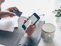Человек, набирающий текст на смартфоне, держа в другой руке банковскую карту