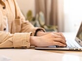 Руки, печатающие на клавиатуре открытого ноутбука, стоящего на светлом столе