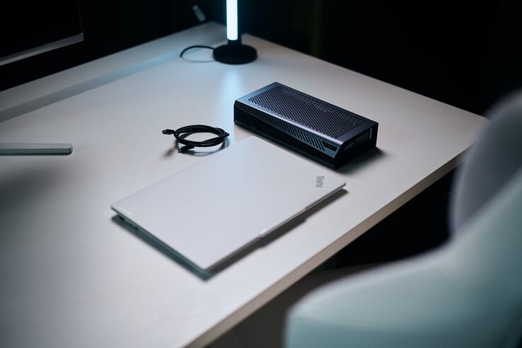Закрытый белый ноутбук ThinkPad, расположенный на столе рядом с компактным внешним графическим модулем Aorus RTX 5060 Ti AI Box и спиральным кабелем Thunderbolt.