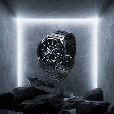 Часы G-Shock GST-B1000BD-1A подвешены над темными камнями в бетонном выставочном зале, подчеркивая черную конструкцию из нержавеющей стали.