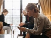 Девушка-подросток смотрит на смартфон, а на заднем плане вне фокуса сидят двое взрослых.