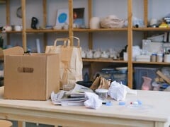 Картонная коробка и бумажные пакеты на деревянном столе в офисе с полками.