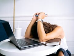 Женщина, смотрящая вниз на свой смартфон, рядом с ней лежит ноутбук