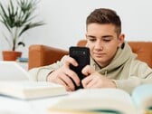 Подросток в толстовке с капюшоном, печатающий на смартфоне, перед ним лежат раскрытые школьные учебники