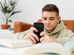 Подросток в толстовке с капюшоном, печатающий на смартфоне, перед ним лежат раскрытые школьные учебники