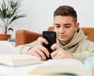 Подросток в толстовке с капюшоном, печатающий на смартфоне, перед ним лежат раскрытые школьные учебники