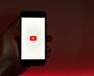 Рука, держащая смартфон с логотипом YouTube, светящимся на дисплее на красном фоне