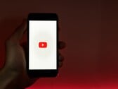 Рука, держащая смартфон с логотипом YouTube, светящимся на дисплее на красном фоне