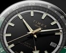 Крупный план чёрного циферблата Timex Atelier GMT Première M1a с золотистыми стрелками, люминесцентными часовыми метками, окошком даты и чёрно-зелёным 24-часовым кольцом GMT.