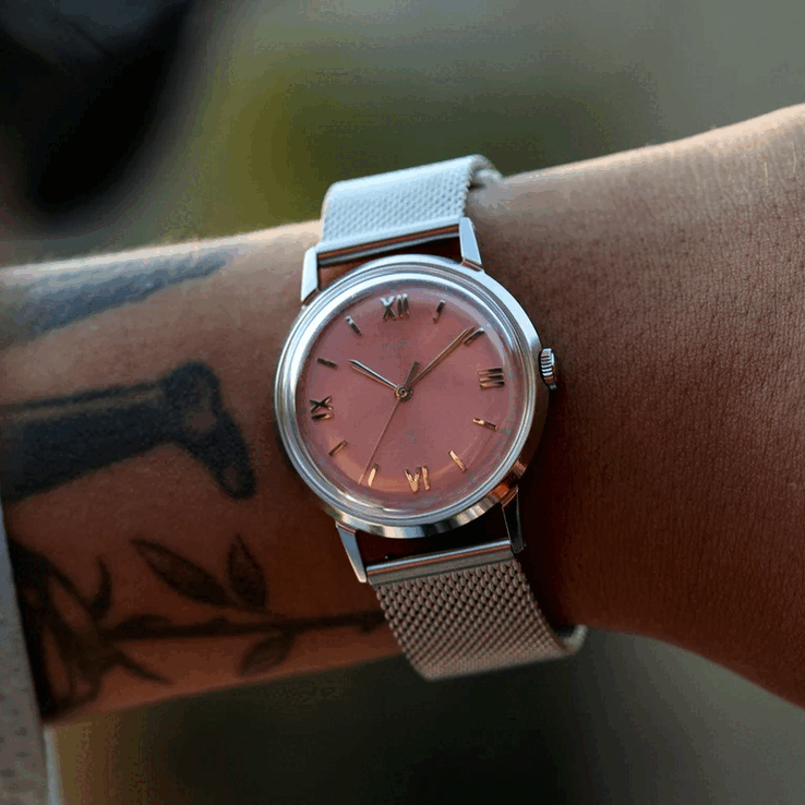 Человек, носящий часы Timex x Todd Snyder Marlin Mesh с циферблатом цвета «лосось» с эффектом «солнечных лучей» и сетчатым браслетом.