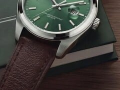 Крупный план часов Timex Legacy Day and Date: зелёный циферблат с отделкой «солнечные лучи», безель серебристого цвета и ушки с матовой шлифовкой, рифлёная заводная головка и фактурный коричневый кожаный ремешок на фоне тёмно-зелёной коробки и деревянной поверхности.