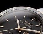 Крупный план часов Timex Waterbury Heritage Automatic с чёрным циферблатом, на котором видны граненые светящиеся стрелки, часовые метки, индикатор дня недели и даты, а также чёрный безель.