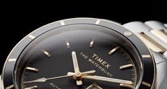Крупный план часов Timex Waterbury Heritage Automatic с чёрным циферблатом, на котором видны граненые светящиеся стрелки, часовые метки, индикатор дня недели и даты, а также чёрный безель.