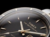 Крупный план часов Timex Waterbury Heritage Automatic с чёрным циферблатом, на котором видны граненые светящиеся стрелки, часовые метки, индикатор дня недели и даты, а также чёрный безель.