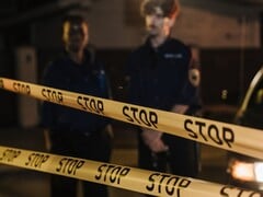 Двое полицейских стоят ночью за жёлтой лентой с надписью «Стоп»