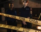 Двое полицейских стоят ночью за жёлтой лентой с надписью «Стоп»