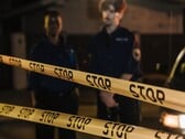 Двое полицейских стоят ночью за жёлтой лентой с надписью «Стоп»