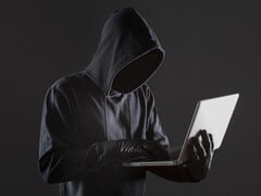 Хакер в капюшоне управляет ноутбуком на темном фоне.