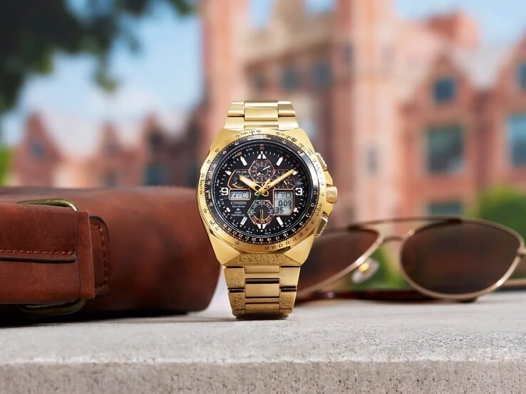 Пилотские часы Citizen Promaster Skyhawk A-T JY8144-50E золотистого цвета, расположенные вертикально на выступе рядом с коричневой кожаной сумкой и солнцезащитными очками, на фоне размытого городского пейзажа.