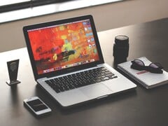 MacBook Pro на тёмном столе рядом со смартфоном, очками и блокнотом