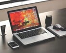 MacBook Pro на тёмном столе рядом со смартфоном, очками и блокнотом