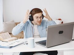 Мужчина в наушниках вскидывает руки от досады перед ноутбуком