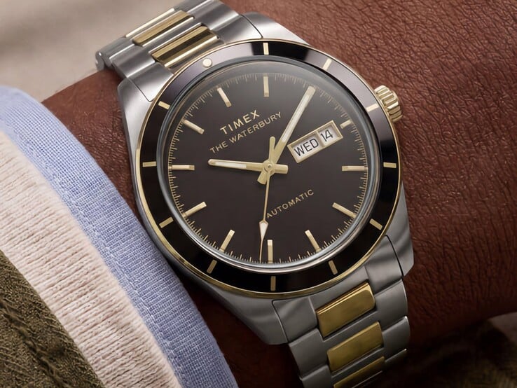 Двухцветные часы Timex Waterbury Heritage Automatic с чёрным циферблатом, надетые на запястье, с видимым указателем дня недели и даты, а также золотистыми акцентами.