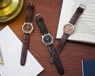 Три часы Citizen Rolan, расположенные на деревянном столе рядом с блокнотом, ручкой, лампой и раскрытой книгой, в том числе модель AW2110-14Z с циферблатом лососевого цвета.