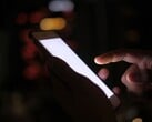 Рука, держащая смартфон со светящимся экраном в темноте