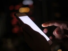 Рука, держащая смартфон со светящимся экраном в темноте