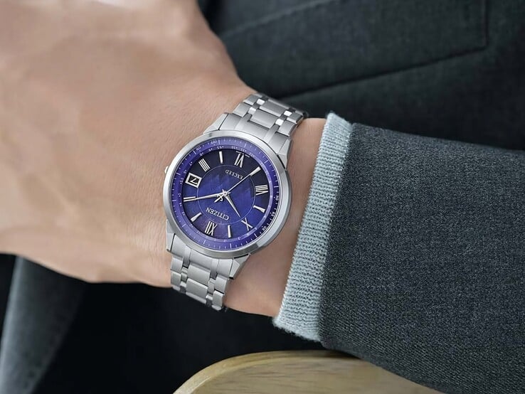 Citizen Exceed CB1140-79L на запястье: синий циферблат, корпус серебристого цвета и интегрированный титановый браслет на фоне тёмного пиджака.