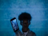 Парящий смартфон с кодом на экране на синем фоне, с размытым человеком позади него