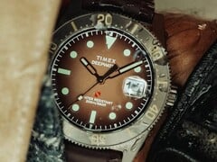 Часы для дайвинга Huckberry x Timex Deepwater Reef 200 с коричневым циферблатом, корпусом из нержавеющей стали, чёрным безелем и ремешком того же коричневого цвета.