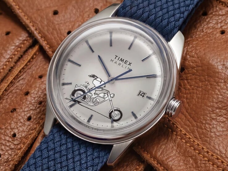 Вид под углом спереди на часы Peanuts x Timex Marlin Jet Automatic Easy Rider, на котором хорошо видны выпуклое стекло, корпус из нержавеющей стали серебристого цвета, циферблат с изображением Снупи и синий тканевый ремешок.