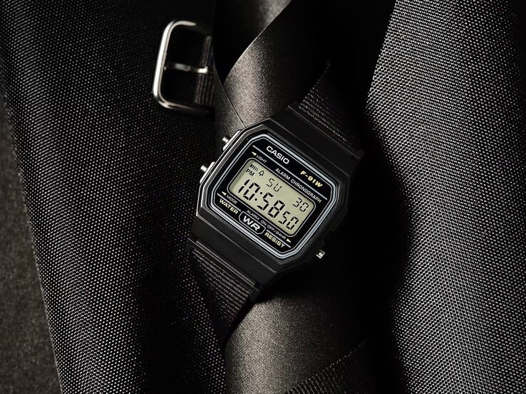 Цифровые часы Casio F-91WF-1A с чёрным корпусом, чёрным ремешком из плетеной ткани и серебристыми акцентами, сфотографированные на тёмном фактурном фоне.